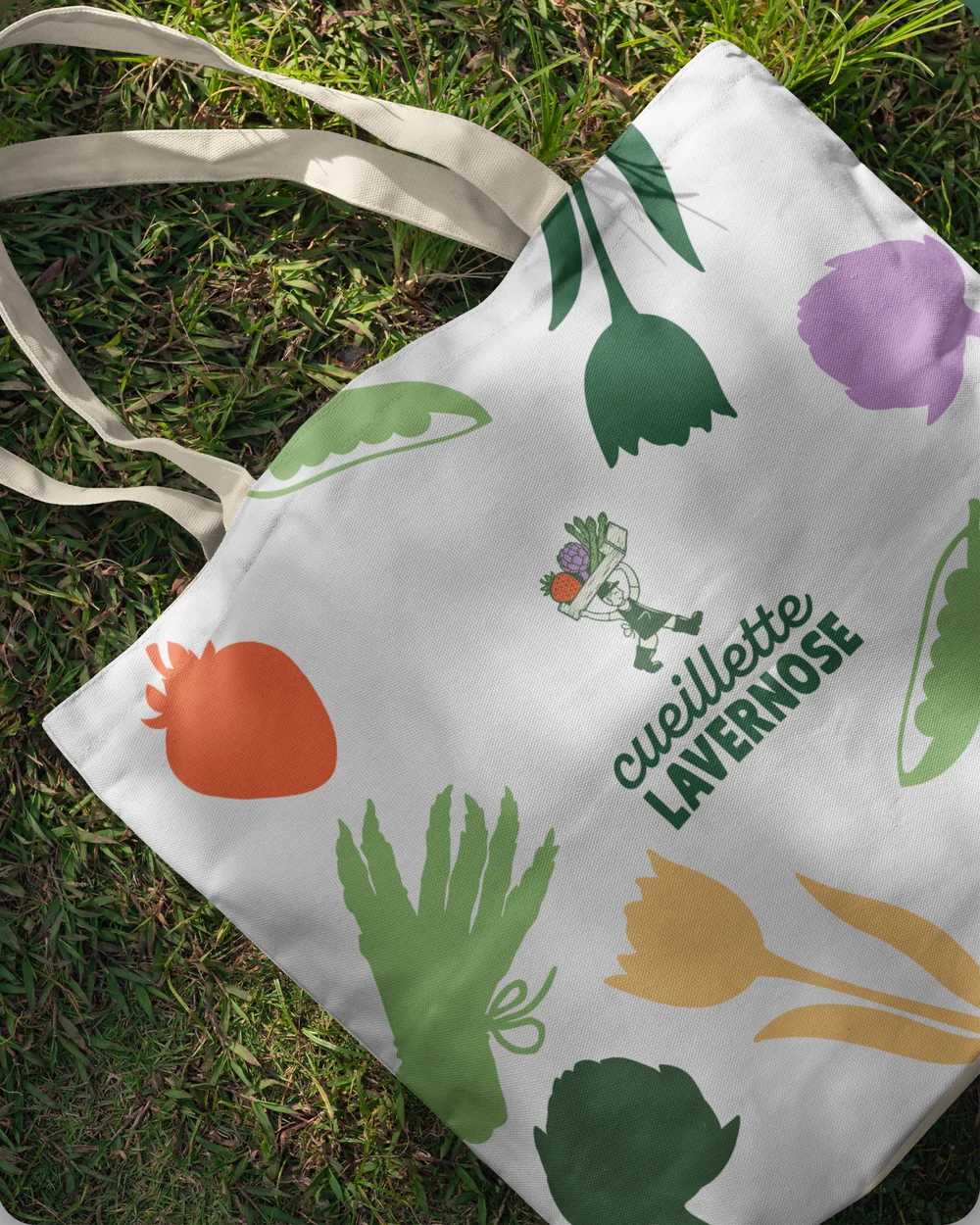 Tote bag aux fruits et légumes en aplats, posé dans l'herbe