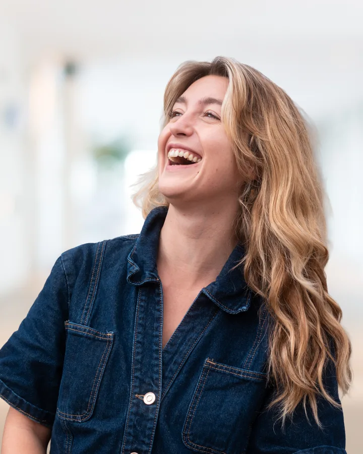 Iona, en veste en jean, éclate de rire