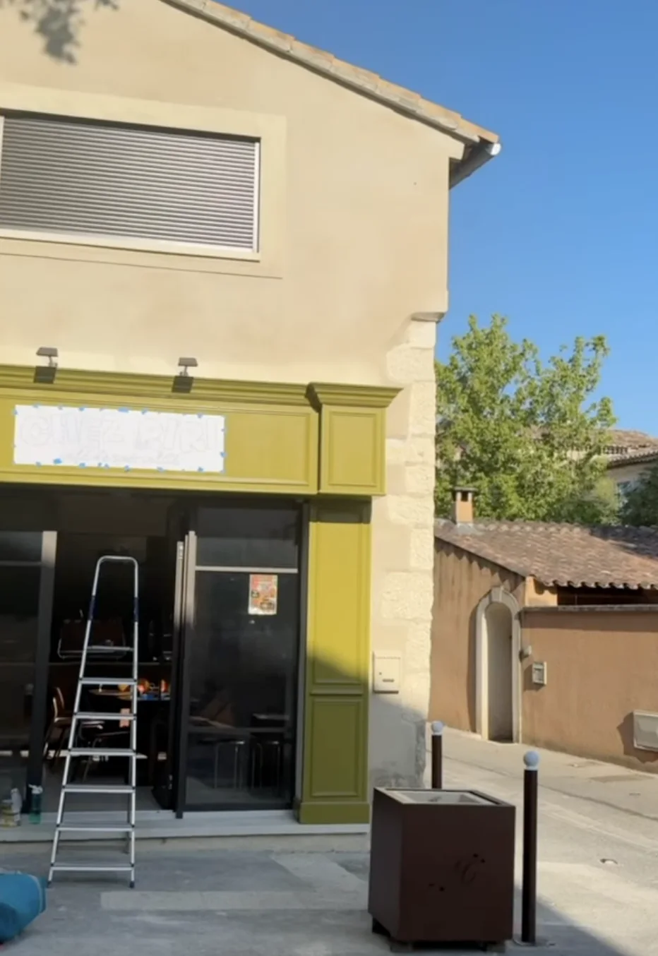 La devanture avant la peinture : le tracé des lettres scotché sur le bandeau, une échelle devant la vitrine