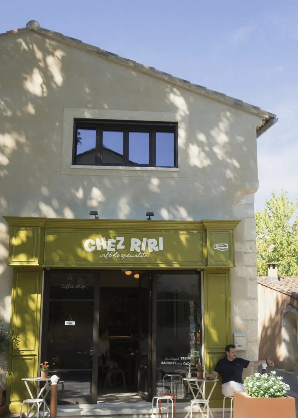 La devanture vert olive de Chez Riri, avec « Chez Riri, café de spécialité » peint en blanc et la terrasse