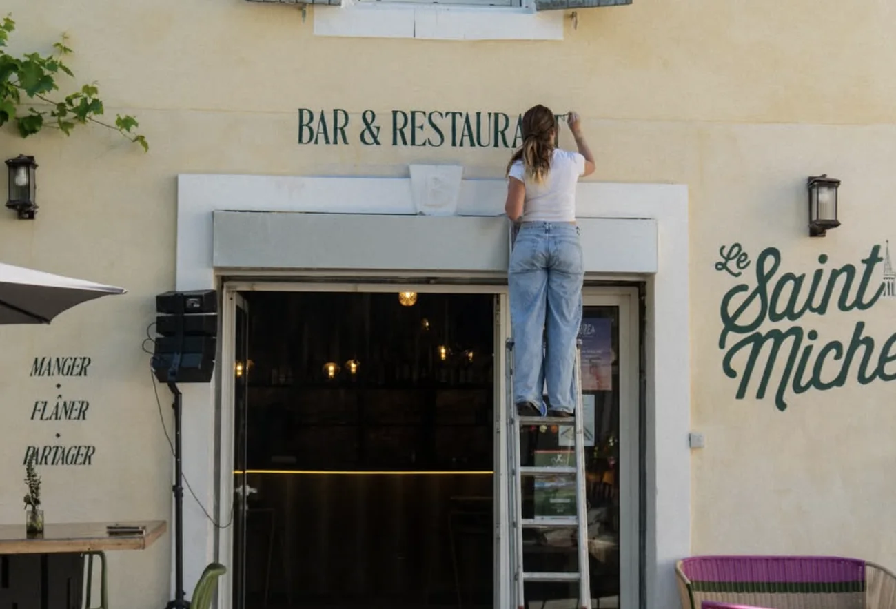 Iona sur l'échelle, en train de peindre la dernière lettre de « Bar & Restaurant »