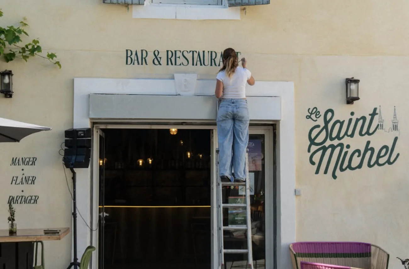 La façade du Saint Michel : Iona sur son échelle peint « Bar & Restaurant » au-dessus de la porte